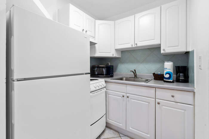 Full kitchen with white cabinets, full-size fridge, stove and coffee maker