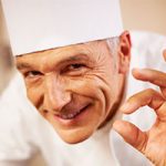 A man in chef 's outfit making an okay sign.