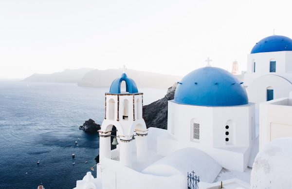 A church with blue domes sits on the shore of an ocean.