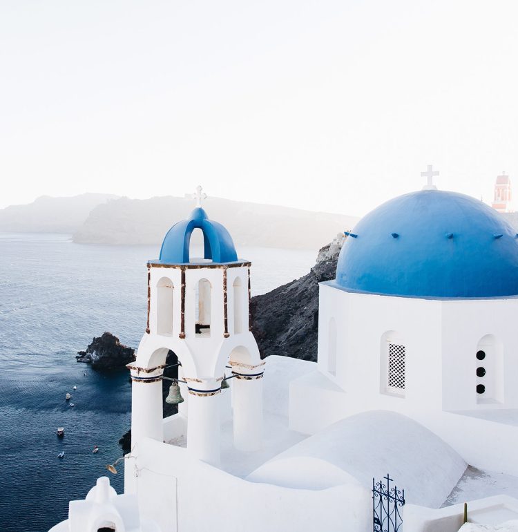 A church with blue domes sits on the shore of an ocean.